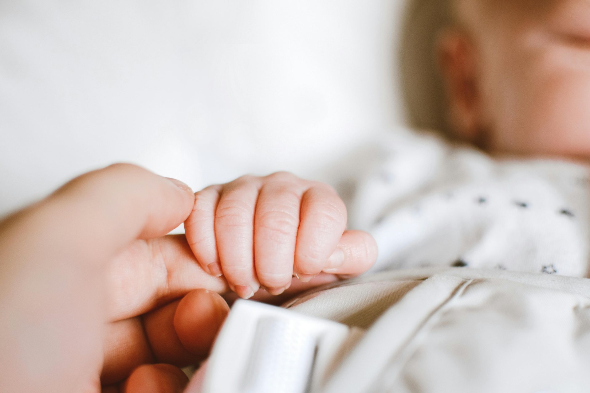 A newborn baby holding an adult’s finger